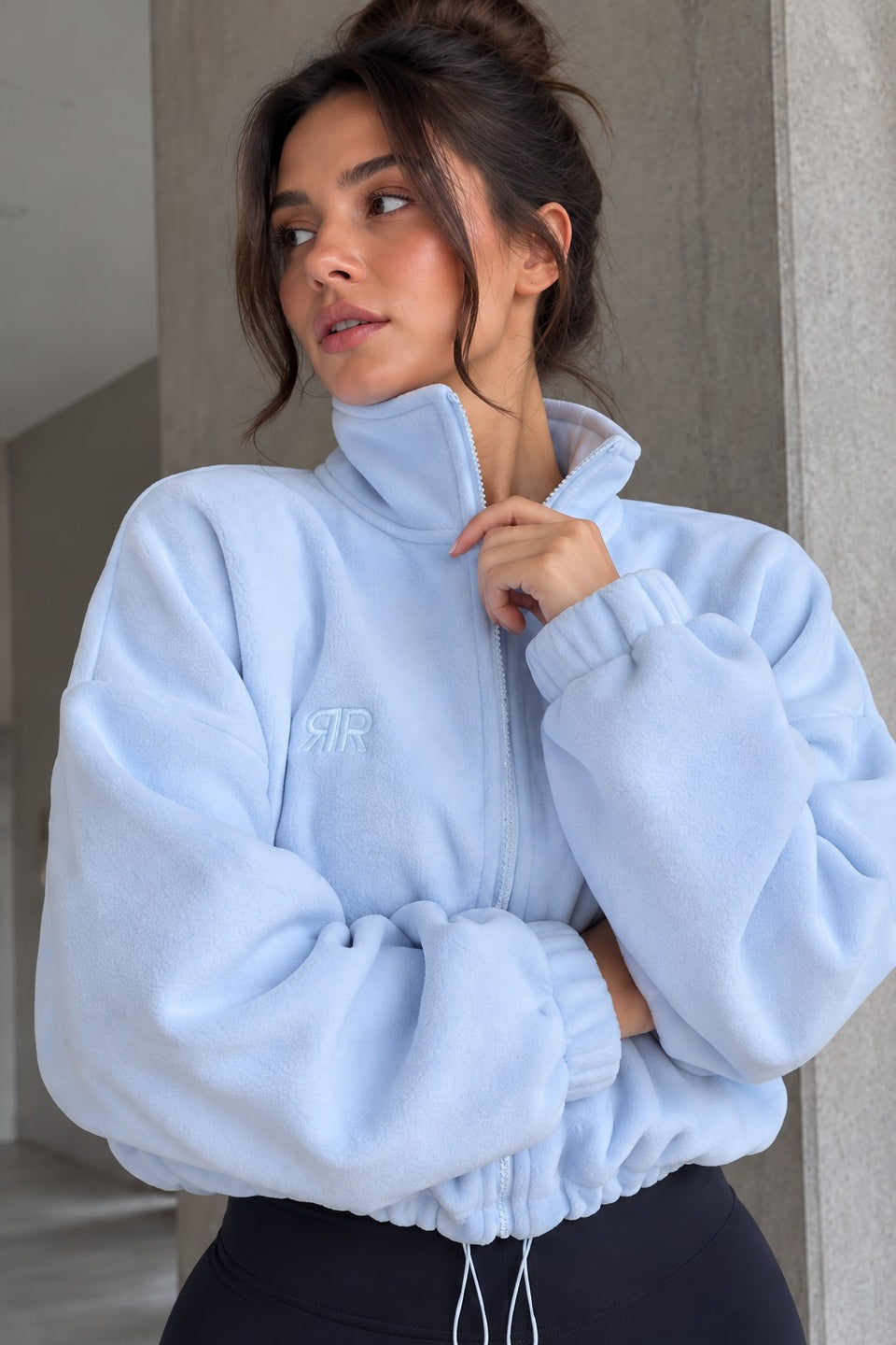 Modelo con la Chaqueta Era azul claro ajustando el cuello alto: cremallera, resorte con cordón y puños con resorte